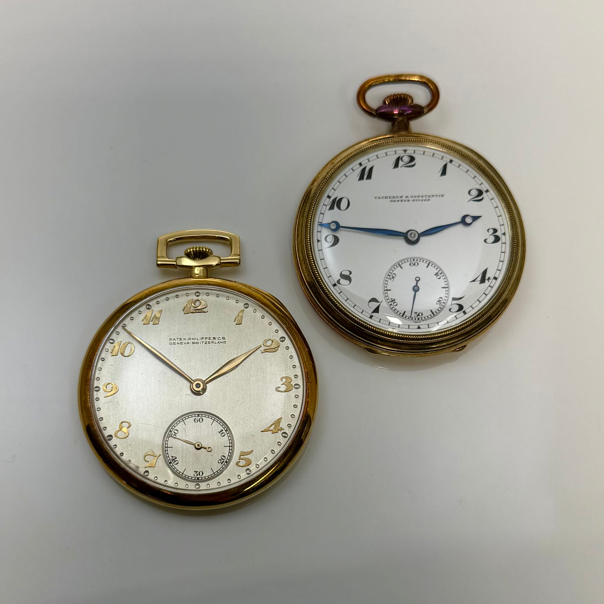 Two pocket watches displayed together, with contrasting numerals and small seconds subdials.